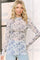 woman wearing a light sheer long sleeve floral top in shades of blue and white with a fitted style
