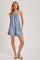 woman wearing a light blue denim romper with adjustable straps and pockets, styled with brown sandals