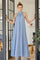woman wearing a light blue halter neck maxi dress standing in a doorway with her hands on the door frame