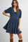 woman wearing a navy blue short sleeve dress with a large collar and ruffle hem, posing casually