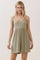 woman wearing a light olive green spaghetti strap mini dress with a fitted bodice and flared skirt