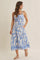 woman wearing a blue and white floral print maxi dress with spaghetti straps and pockets, smiling against a light background