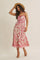 woman wearing a floral print pink and white maxi dress with a fitted bodice and a flowy skirt, accessorized with a straw hat