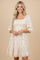 woman wearing a beige floral embroidered puff sleeve mini dress with a smocked bodice and lace trim