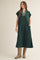 woman wearing a dark green oversized dress with a collared neckline and pockets, paired with beige cowboy boots