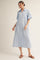 woman wearing a light blue button-up shirt dress with rolled sleeves and a front pocket, standing in a relaxed pose