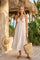woman wearing a white halter neck maxi dress with tiered detailing, standing in a tropical setting with a woven tote bag