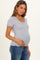 woman wearing a grey maternity top with a scoop neckline and short ruffled sleeves, holding her baby bump