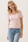 woman wearing a light pink short sleeve knit top with ruffled cuffs and button details, smiling while standing