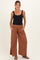 woman wearing a black tank top and rust wide-leg maternity pants, standing with hands on hips