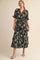 woman wearing a black floral maxi dress with ruffled sleeves and a tie waist, standing in a neutral background
