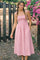 woman wearing a pink gingham smocked maxi dress with adjustable straps and pockets, standing outdoors among flowers