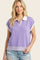 woman wearing a lilac short sleeve polo sweater with a white collar and striped hem, paired with distressed denim shorts