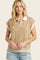 woman wearing a beige short sleeve polo sweater with a white collar and striped hem, styled with distressed denim shorts
