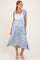 woman wearing a light blue maternity dress with floral patterns and tie straps, styled with a flowy skirt and white sandals