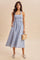 woman wearing a light blue striped halter dress with a smocked bodice and a full skirt, holding a small woven bag