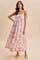 woman wearing a floral maxi dress with pink and white tones and thick straps, standing against a neutral background