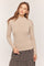 woman wearing a beige long sleeve fitted top with a scalloped hem and styled with a checkered skirt