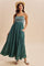 woman wearing a dark green maxi dress with a smocked bodice and ruffled hem, accessorized with a straw hat