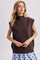 woman wearing a brown sleeveless mock neck sweater styled over a blue polka dot skirt