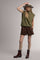 woman wearing an olive green sleeveless sweater, brown suede shorts, and brown ankle boots, with a wide-brim hat