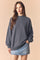 woman wearing a dark gray oversized sweatshirt with a high neck and long sleeves paired with a denim skirt