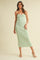 woman wearing a light green strapless midi dress with a twist front detail and posing against a beige background