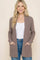 woman wearing a tan ribbed cardigan with pockets over a white top and blue jeans