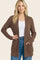 woman wearing a brown ribbed cardigan with pockets over a white top and high-waisted jeans