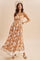 woman wearing an orange floral maxi dress with a square neckline and straps, posing stylishly with a wide-brimmed hat