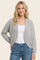 woman wearing a light gray cropped cardigan over a white tank top and blue jeans