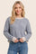 woman wearing a grey striped knit sweater with beige cuffs and holding her hands at her waist