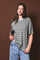 woman wearing a striped oversized t-shirt in blue and beige with jeans against a brown background