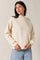 woman wearing a cream-colored long sleeve sweatshirt with a mock neck and relaxed fit, paired with light blue jeans