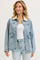 woman wearing a light blue denim jacket with a cream collar and front pockets, styled with a white top and light jeans