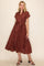 woman wearing a rust-colored midi dress with white polka dots and a waist tie, standing on a neutral background