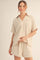 woman wearing a beige short sleeve top with a v-neck and matching shorts, relaxed fit and subtle texture