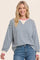 woman wearing a striped blue and white oversized sweatshirt with pink and white trim, smiling while posing
