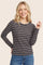 woman wearing a navy striped long sleeve top with light pink and grey stripes, smiling and posing with a hand raised