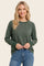 woman wearing a green long sleeve raglan sweatshirt with ribbed cuffs and a relaxed fit, paired with blue jeans