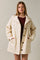 woman wearing a cream oversized jacket with button front and side pockets over a maroon top