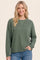 woman wearing a green waffle knit long sleeve top paired with blue jeans, smiling at the camera