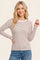 woman wearing a cream and brown striped long sleeve top, smiling and posing with one hand on her hip