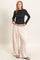 woman wearing a black long sleeve top with asymmetrical design and light beige wide-leg pants with drawstring waist
