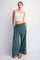 woman wearing a white crop top and teal wide-leg pants with pockets and drawstring waist