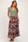 woman wearing a green ribbed maternity top and a long floral maternity maxi skirt, holding her baby bump