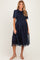 woman wearing a navy maternity dress with floral print and sheer puff sleeves, holding the skirt to show off the baby bump