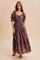 woman wearing a brown floral maxi dress with puff sleeves and pockets, standing against a neutral backdrop