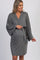 woman wearing a gray maternity wrap dress with wide sleeves and a tie waist, gently holding her baby bump