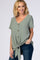 woman wearing a sage green short sleeve top with a button front and a tied hem, paired with dark blue jeans